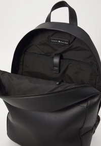 Sac à dos en cuir noir avec compartiment principal ouvert montrant une poche intérieure et une étiquette avec la marque Tommy Hilfiger.