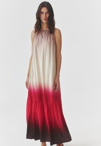 Robe maxi en satin avec un design sans manches, présentant un dégradé allant de la crème au rouge profond, et un ourlet volé avec un bas noir.