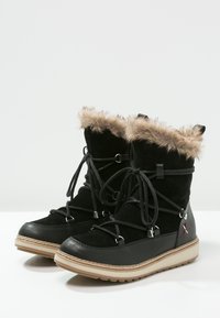 Botas de invierno negras con borde de piel sintética, textura de ante, punta redondeada y detalles decorativos de cordones. Suela de goma con un borde beige.