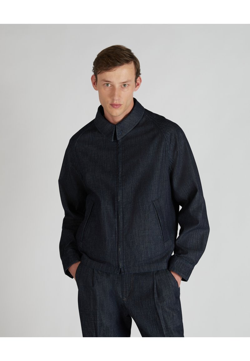 Veste en denim foncé avec col, fermeture éclair sur le devant et poches latérales. Le tissu a une texture subtile et est assorti à un pantalon coordonné.