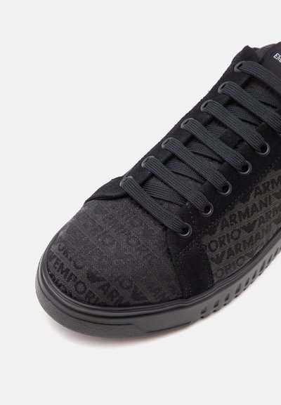 Baskets noires avec tige en tissu présentant un motif de texte répétitif "Armani" et lacets noirs sur une semelle en caoutchouc texturée.