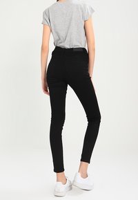 Jeans negros ajustados con tiro alto, combinados con una camiseta de manga corta gris y zapatillas blancas. Tejido suave y diseño ajustado.