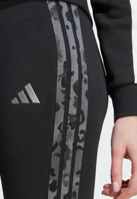 Black athletic leggings featuring textured black and gray animal print side stripes, metallic logo, and smooth fabric finish.