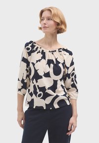 Blůza s navy a krémovým vzorem, tříčtvrtečním rukávem, shromážděným výstřihem a měkkou strukturou. Obsahuje výrazné abstraktní tvary a uvolněný střih.