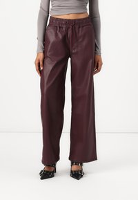Burgundske široke hlače iz umetnega usnja z elastiko in vrvico. Gladka tekstura z sijočim zaključkom.