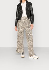 Chaqueta de motociclista de cuero negro sobre una blusa blanca, combinada con pantalones beige de pierna ancha con estampado de leopardo y zapatillas de color claro.