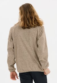 Brun heathered tröja med avslappnad passform, långa ärmar, resårkanter och utan synliga knäppningar, bärs över mörka byxor.