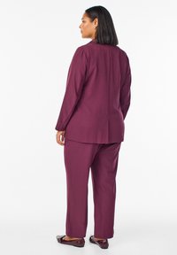 Traje burdeos a medida con una chaqueta estructurada y pantalones de pierna recta. Tela suave con un brillo sutil, que presenta detalles de diseño minimalistas.