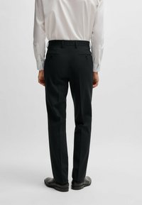 Pantaloni neri su misura con taglio dritto, dotati di due tasche posteriori e una texture liscia, abbinati a una camicia bianca a maniche lunghe.