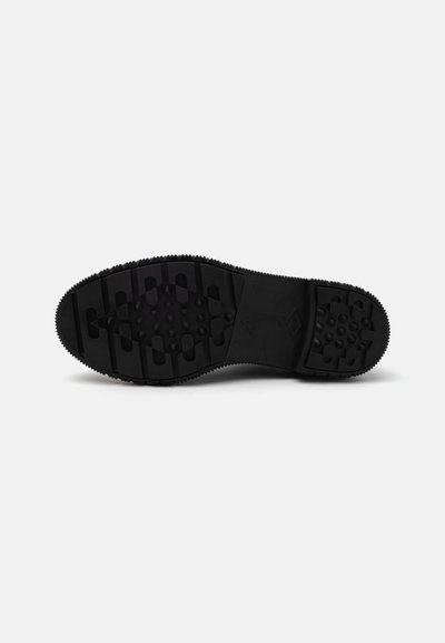 Black rubber shoe sole featuring a textured surface with various patterns, including ridges and circular grips for traction.