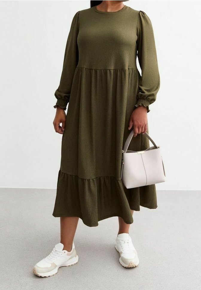 Robe vert olive à manches longues avec un tissu texturé, jupe à volants et poignets froncés ; associée à des sneakers blanches et beiges et un sac à main léger.