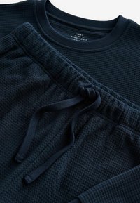 Granatowy, teksturowany sweter z bawełny oraz pasujące spodnie dresowe z elastycznym pasem i detalem w postaci sznurka. Klasyczny krój.