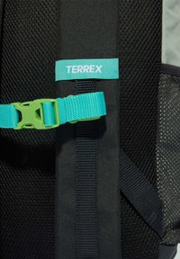 Čierny batoh Terrex s textúrovaným sieťkovým panelom, tyrkysovým nastaviteľným popruhom a štítkom. Disponuje bezpečnou prackou a spevnenými švami.