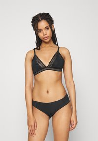 Schwarzes Wäsche-Set mit einem Spitzenborte-Bralette mit verstellbaren Trägern und passenden nahtlosen Slips, beide aus weichem Material gefertigt.