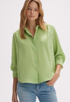 Camicia button-up verde chiaro con un motivo testurizzato, caratterizzata da un colletto e maniche arrotolate, abbinata a jeans blu.