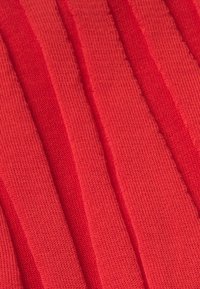 Žebrovaná červená textília s alternujúcimi hladkými a textúrovanými sekciami, ukazujúca jemný pletený vzor a konzistentnú farbu po celom povrchu.