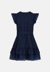 Navy sinivihreä pilkullinen mekko, joka on valmistettu kevyestä kankaasta. Mekossa on lyhyet röyhelöhihoja, istuva vyötärö ja kerrostettu hameen muotoilu.
