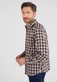 Camicia a quadri marrone e blu realizzata in tessuto, con colletto, chiusura anteriore a bottoni e taschino sul petto. La camicia ha maniche lunghe.