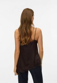 Czarna satynowa koszulka na cienkich ramiączkach z koronkową lamówką, o luźnym kroju. Noszona z ciemnoniebieskimi dżinsami, widziana od tyłu.