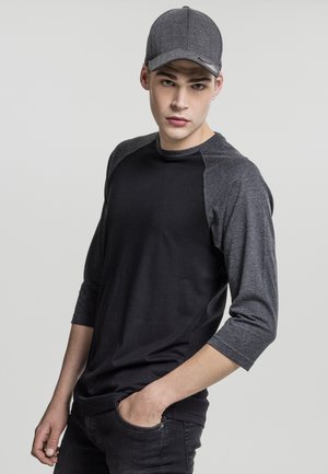 Black and dark gray shirt with three-quarter sleeves, made of cotton, paired with a gray herringbone cap, displayed against a light background.