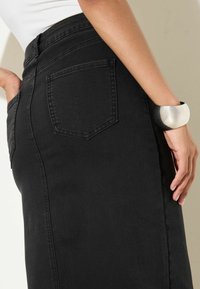 Mustast teksast seelik, millel on liibuv lõige, kõrge talje ja tagataskud. Paremal randmel on lai hõbedane ja must mansetinöör käevõru.