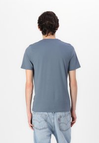Grå bomull t-skjorte med korte ermer, rund hals, ensfarget design og en avslappet passform. Brukt med lyseblå denimjeans. Bakside.