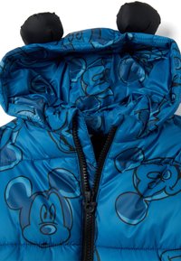 Blauwe pufferjack met zwart Mickey Mouse-patroon, voorzien van een capuchon met ronde zwarte oortjes en een rits aan de voorkant. Gladde, glanzende textuur.