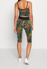 Top corto nero e leggings capri con testo multicolore "Nike" e "Pain" in un motivo a righe verticali, con un design aderente e vita elastica.