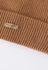 Brown ribbed knit beanie with a leather patch labeled "BELLEMERE NEW YORK." Soft texture, warm material, and fitted design.