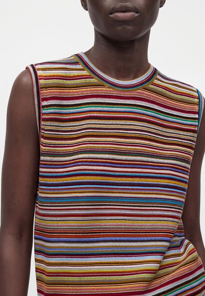 Personne portant un haut en maille sans manches avec des rayures horizontales multicolores en rouge, jaune, bleu, marron et blanc sur fond blanc.