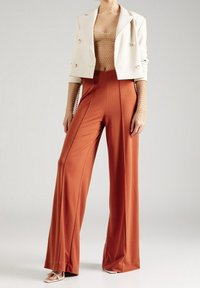 Bruna vida byxan med vertikala sömmar kombineras med en åtsittande nudefärgad nättröja med långa ärmar och en krämfärgad dubbelknäppt blazer.