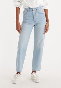 Jeans de cintura alta, de cor azul clara, com perna reta, apresentando cinco bolsos e fecho de botão, combinados com ténis brancos.