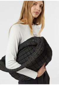 Czarna pikowana torba na ramię o teksturowanej powierzchni, z szerokim paskiem i zamkiem błyskawicznym. Tkanina wydaje się miękka i wyściełana.