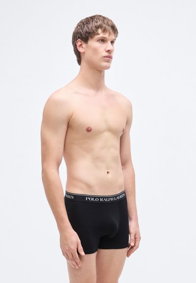 Svarte bomullsboxershorts med bred elastisk linning som har "Polo Ralph Lauren"-logoen. Modellen står nøytralt og viser passform og design.