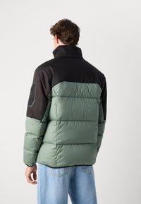 Gevoerde jas met een zwarte bovenkant en groene onderzijde. Heeft een hoge kraag, een gestructureerde afwerking en een rechthoekig logopatch op de mouw.