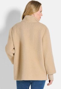 Beige oversized wollen blend jas met een hoge kraag, gestructureerd visgraatpatroon, verlaagde schouders en geribbelde manchetten.