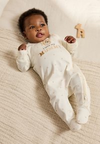 Kreemika värvi uneülikond tähemustritega, millel on lõvi motiiv ja tekst "Ma armastan oma EMAT", luku ja jalalabadega.