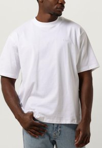 Vit bomullströja med rundad halsringning, korta ärmar och broderad logotyp på framsidan. Kombinationen med ljusblå denimjeans.