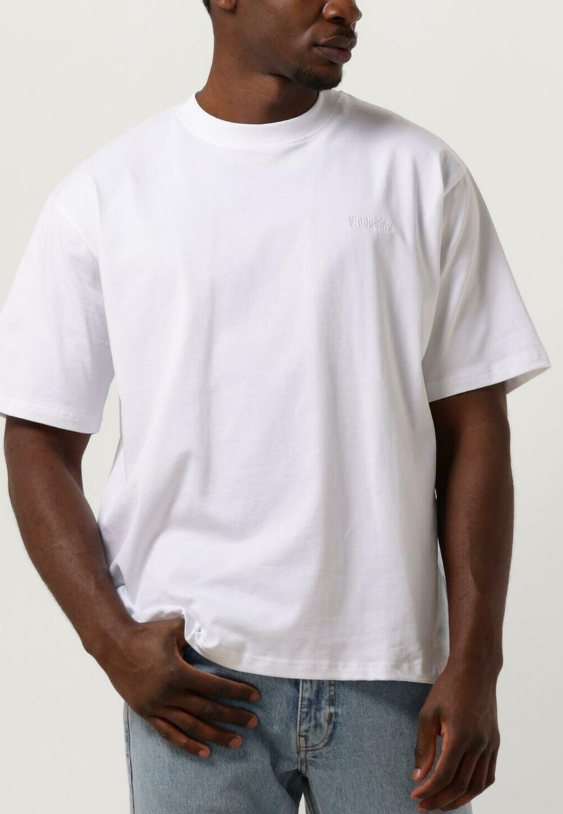 Vit bomullströja med rundad halsringning, korta ärmar och broderad logotyp på framsidan. Kombinationen med ljusblå denimjeans.