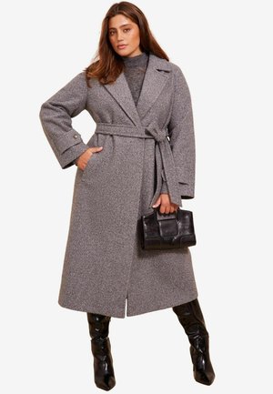 Šedý vlněný trench coat s širokými rukávy, páskem v pase, bočními kapsami a rovný lem. V kombinaci s lesklými černými vysokými botami po kolena.