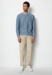 Hellblau strukturierter Pullover mit rundem Halsausschnitt, kombiniert mit beigen Hosen und weißen Sneakern, vor einem schlichten Hintergrund stehend.