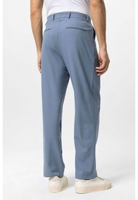 Lichtblauwe broek gemaakt van gladde stof, met een rechte snit, twee achterzakken en een nette tailleband. Gecombineerd met witte sneakers.