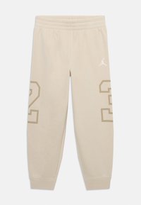 Bežové tepláky vyrobené z mäkkého materiálu s elastickým pásom. Na ľavej nohe majú veľký béžový potlač "23" a biele logo na pravej nohe.