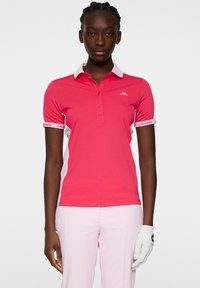 Anpassad rosa polo med klassisk krage, vita sidodetaljer och logotyp på bröstet och ärmarna. Materialet är mjukt och lätt.