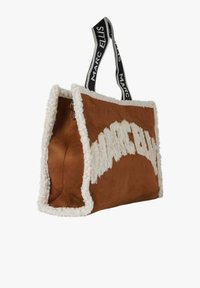 Braune Wildleder-Shopper-Tasche mit weißem Fleecebesatz, einem großen weißen Logo und kontrastierenden schwarzen Griffen mit Markenbeschriftung.