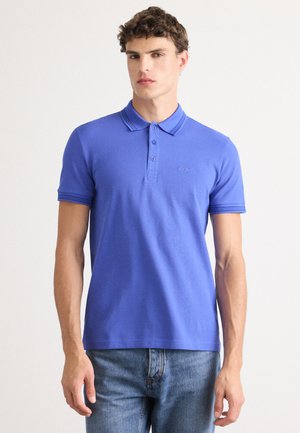 Polo bleu en tissu côtelé, avec un col à trois boutons, des manches courtes, et un petit logo sur la poitrine gauche.