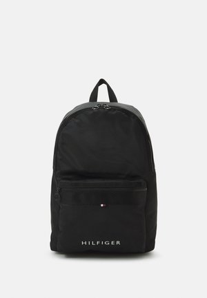 Zaino in nylon nero con forma arrotondata, dotato di una tasca frontale con zip, manico superiore e logo bianco "HILFIGER". Accentuato con una striscia con logo.