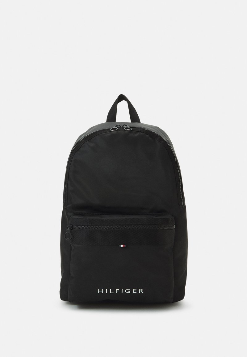 Zaino in nylon nero con forma arrotondata, dotato di una tasca frontale con zip, manico superiore e logo bianco "HILFIGER". Accentuato con una striscia con logo.