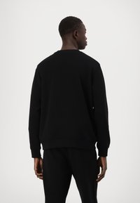 Črna majica s dolgimi rokavi, krožnim ovratnikom, rebrastimi manšeti in robom. Gladka tekstura tkanine, minimalističen dizajn in brez vidnih logotipov.