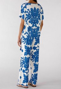 Hvidt outfit med stort blåt blomstermønster. Løs pasform på toppen med korte ærmer. Bukser med bred ben, der matcher toppen, med lignende designs og let flydende tekstur.